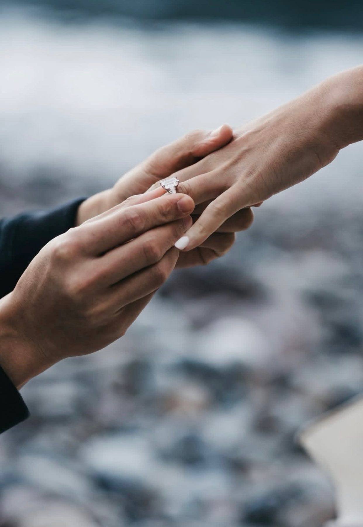 A proposal moment, a diamond ring slipped onto a hand by the coast